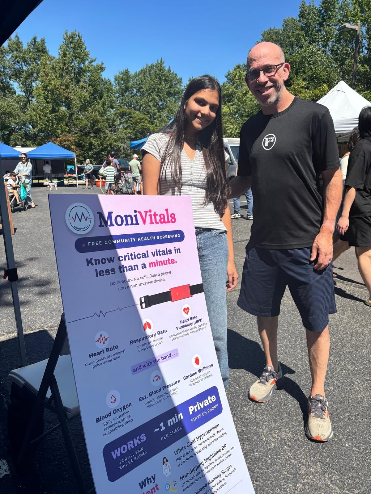 Two people beside the MoniVitals free community health screening board